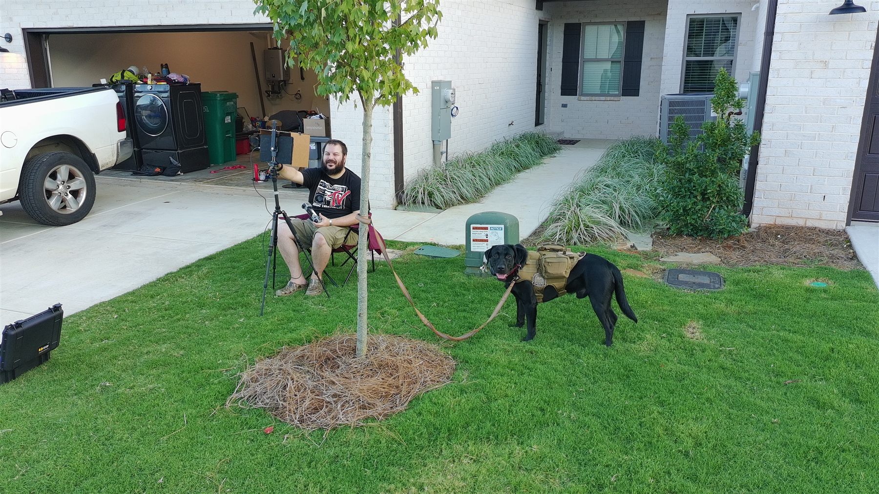 Spencer Callicott flying a drone outside to capture footage of a friend's new townhouse, with Zulu on a leash nearby