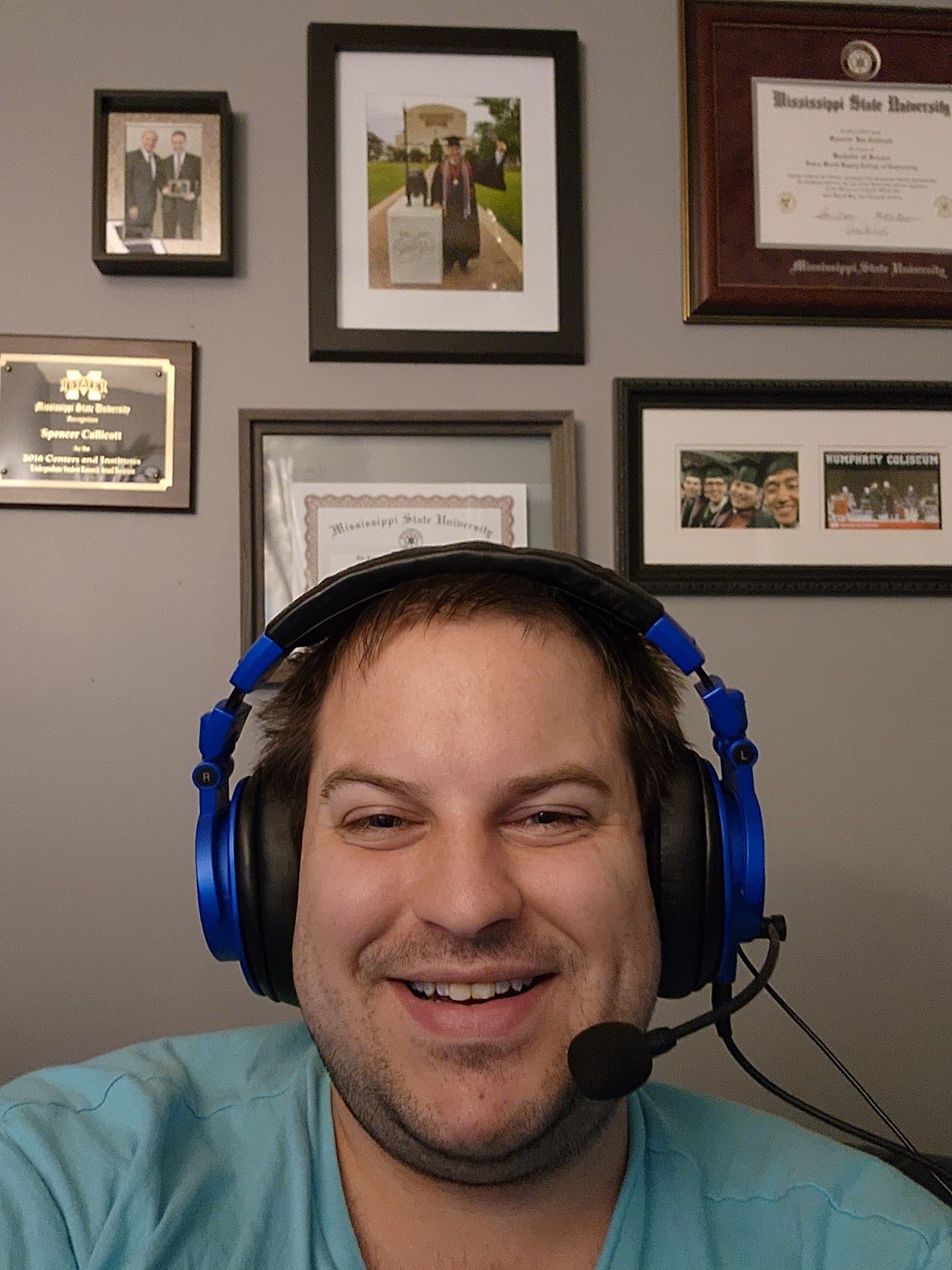 Spencer Callicott in gaming headset in front of wall of MSU diplomas and awards