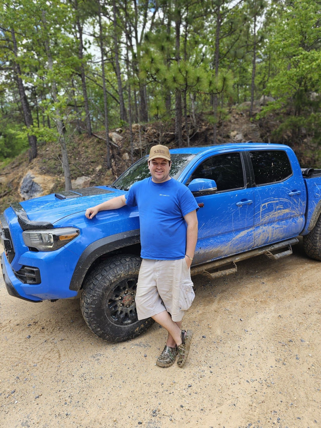 Spencer Callicott next to his muddy blue Toyota Tacoma on a forest trail